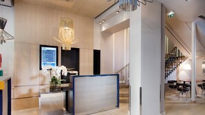 Un área de recepción moderna con una pantalla digital, un mostrador de recepción y una escalera que conduce a pisos superiores.