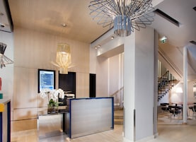 Un área de recepción moderna con una pantalla digital, un mostrador de recepción y una escalera que conduce a pisos superiores.