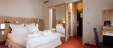 A hotel room with a large bed, a mirror, a desk, and a red patterned carpet.