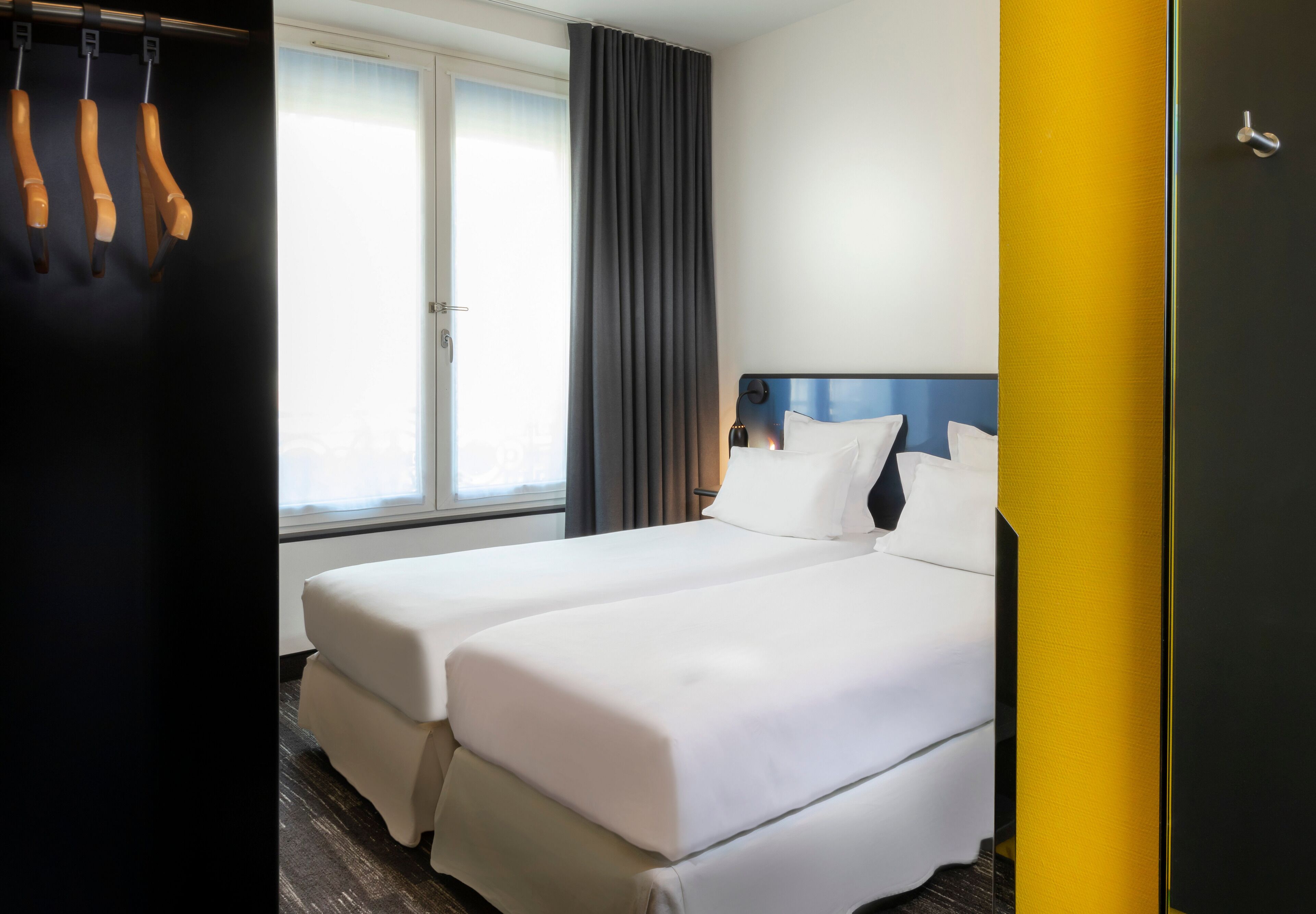 A hotel room with two beds, a wardrobe, and a window with curtains.