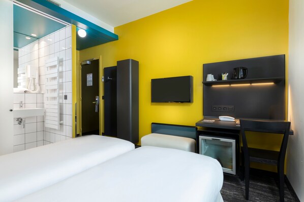 A hotel room with two beds, a desk, a TV, and a mini-fridge.