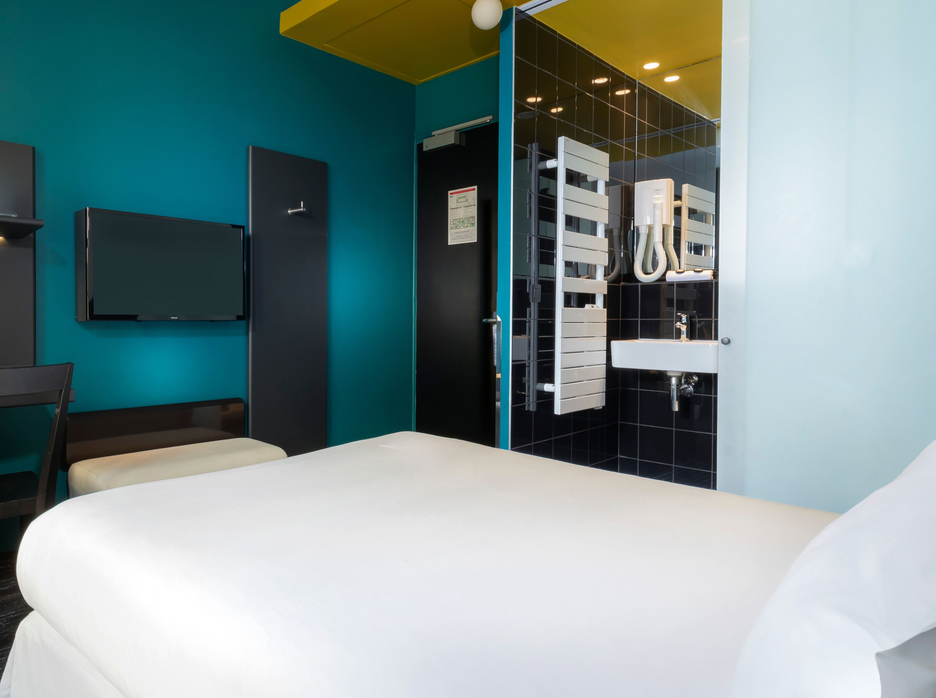 Una habitación de hotel moderna con cama, escritorio, televisor y baño con lavamanos y ducha.