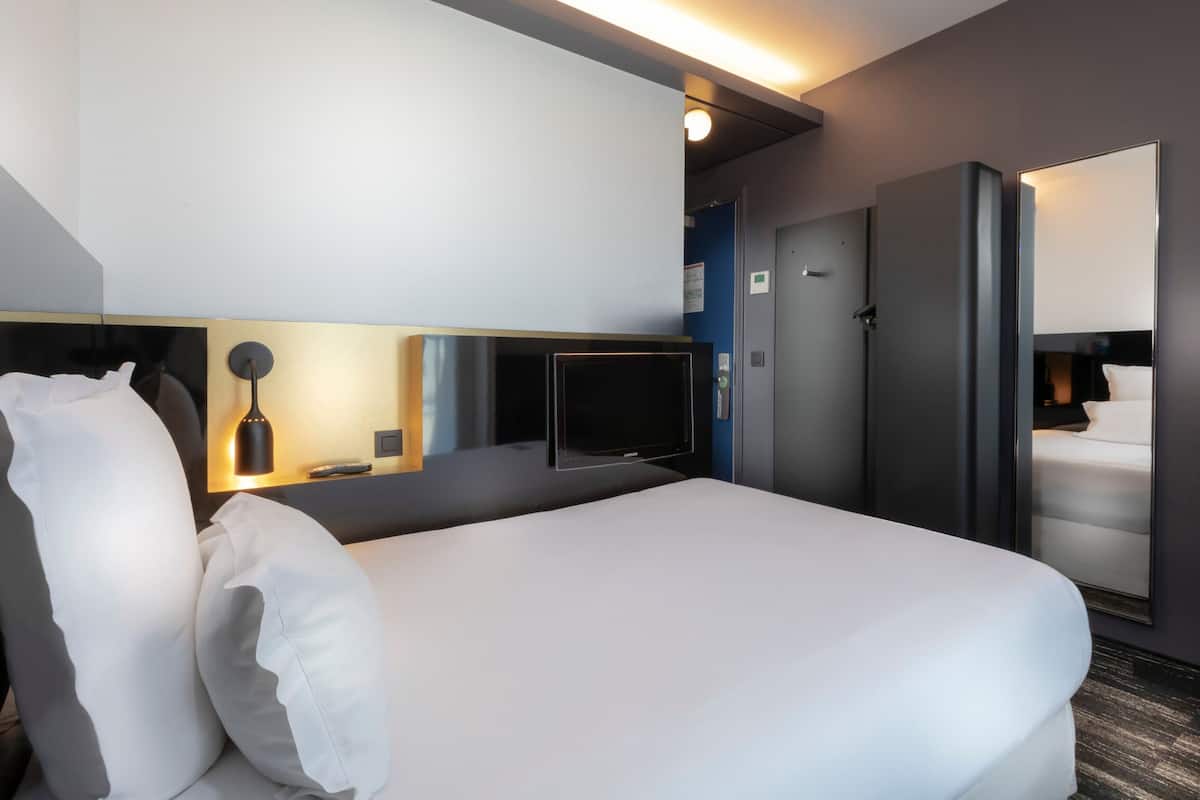 Una habitación de hotel moderna con una cama grande, un televisor de pantalla plana, un minibar y un espejo.