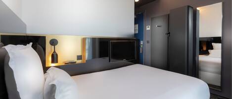 Una habitación de hotel moderna con una cama grande, un televisor de pantalla plana, un minibar y un espejo.