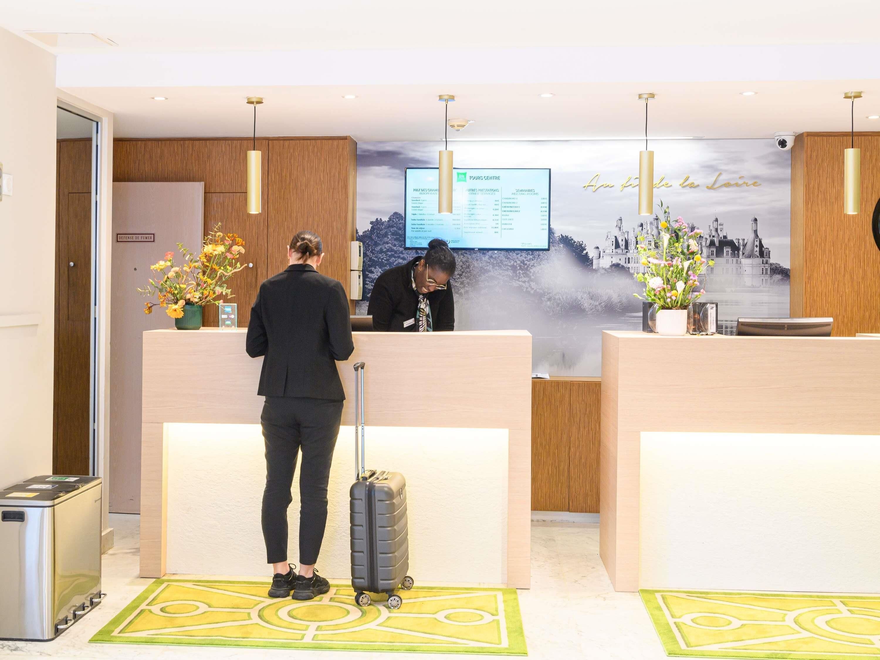 Un mostrador de recepción con una pantalla digital que muestra información, paneles de madera y una vista de un castillo a través de una ventana brumosa.