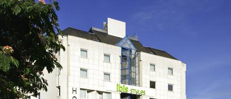 A hotel with a modern design, featuring a prominent 'ibis styles' sign, multiple windows, and a corner entrance.