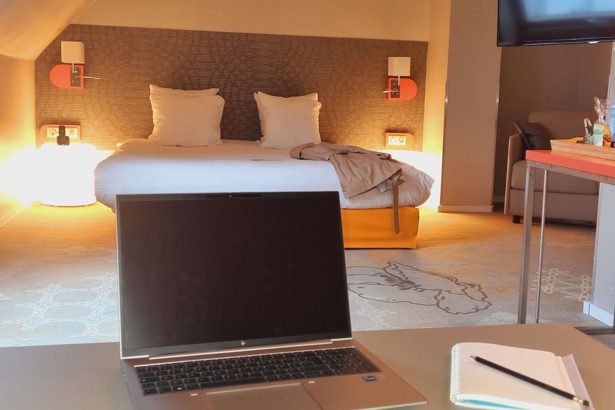 Une chambre d’hôtel avec un lit, un bureau équipé d’un ordinateur portable, d’un carnet et d’un stylo.