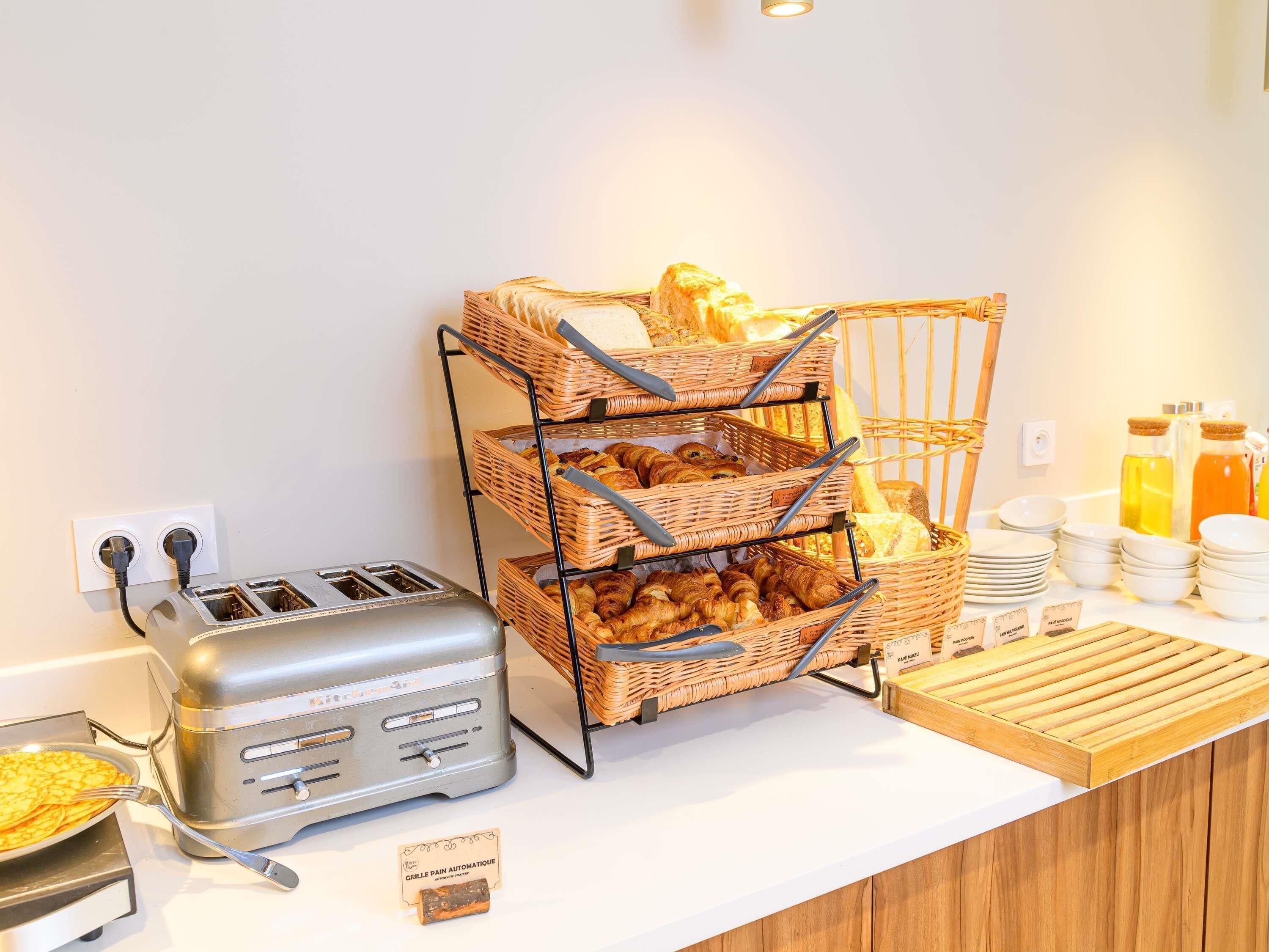 Un buffet de petit-déjeuner comprenant un grille-pain, des paniers en osier remplis de viennoiseries et un plateau de service en bois.