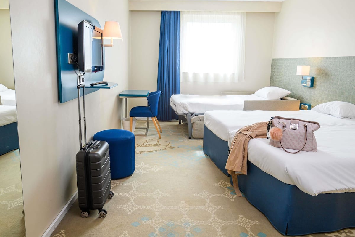 A hotel room with two beds, a desk, a chair, a TV, and a suitcase.
