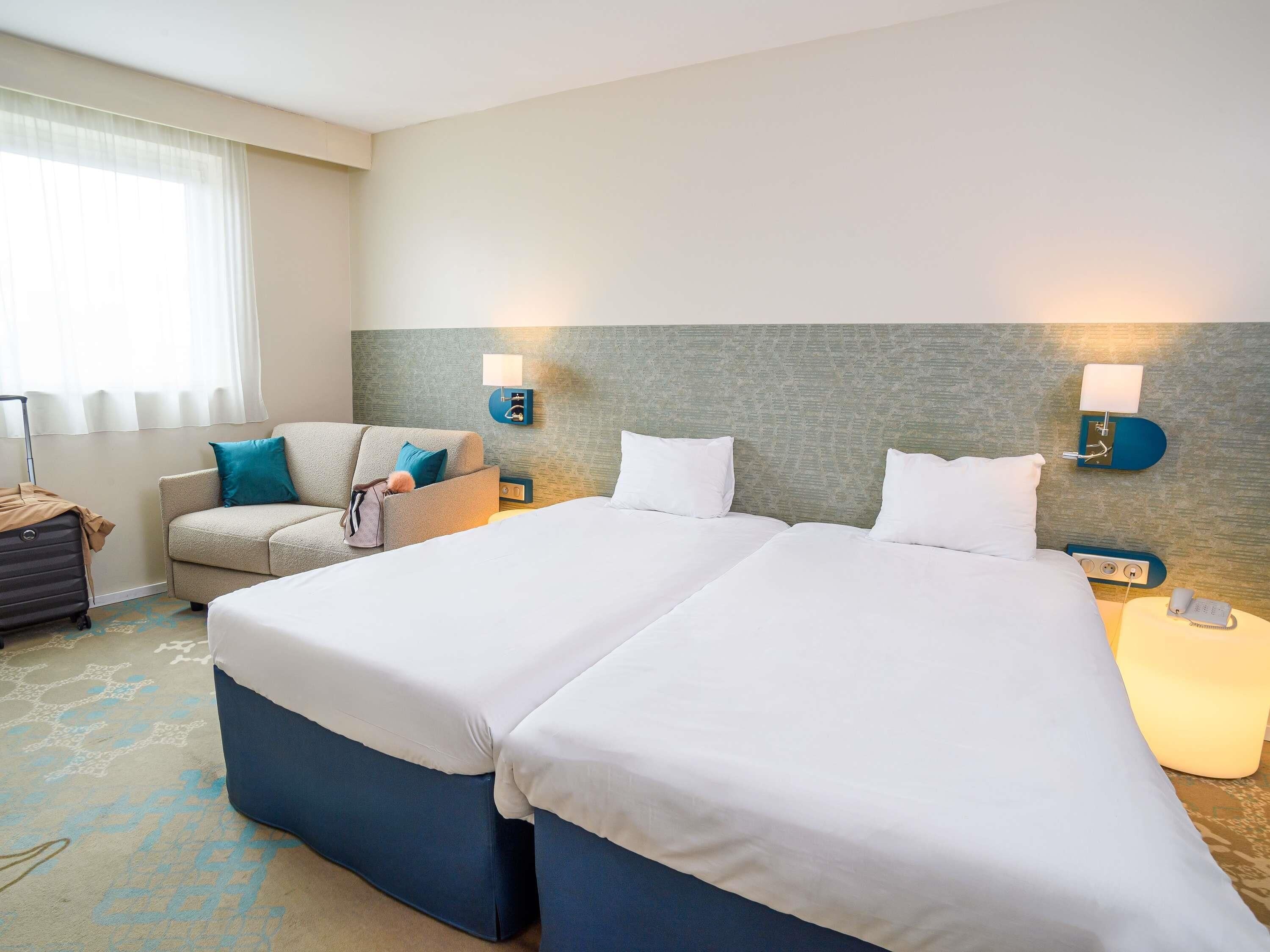 A hotel room with a bed, a sofa, a lamp, and a suitcase.
