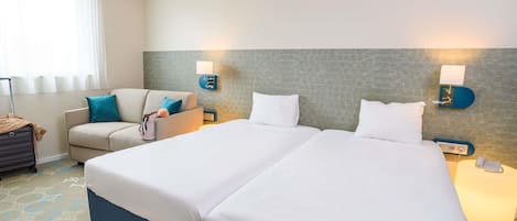 A hotel room with a bed, a sofa, a lamp, and a suitcase.
