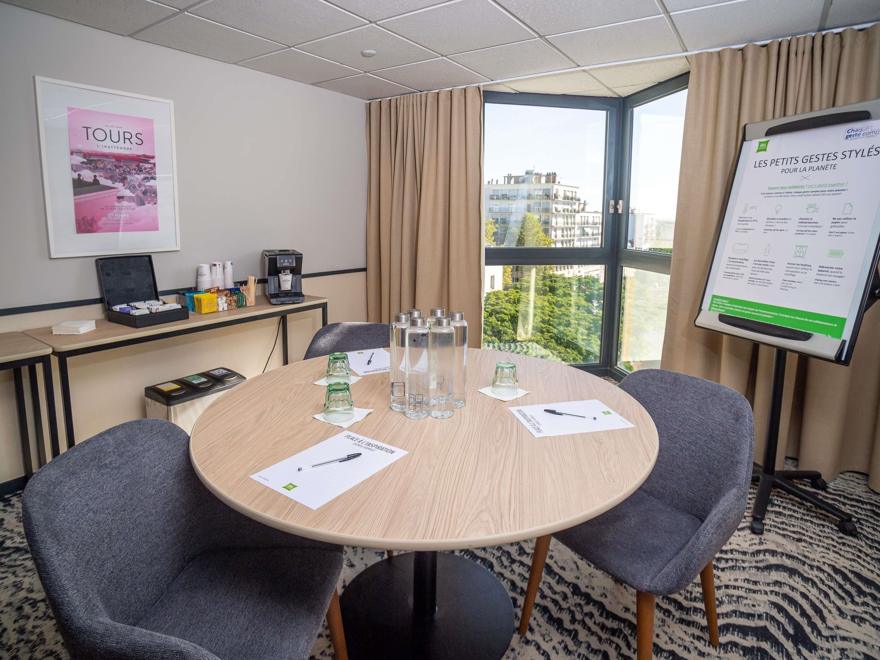 A conference room with a round table, two chairs, a projector screen, and a window with a city view.