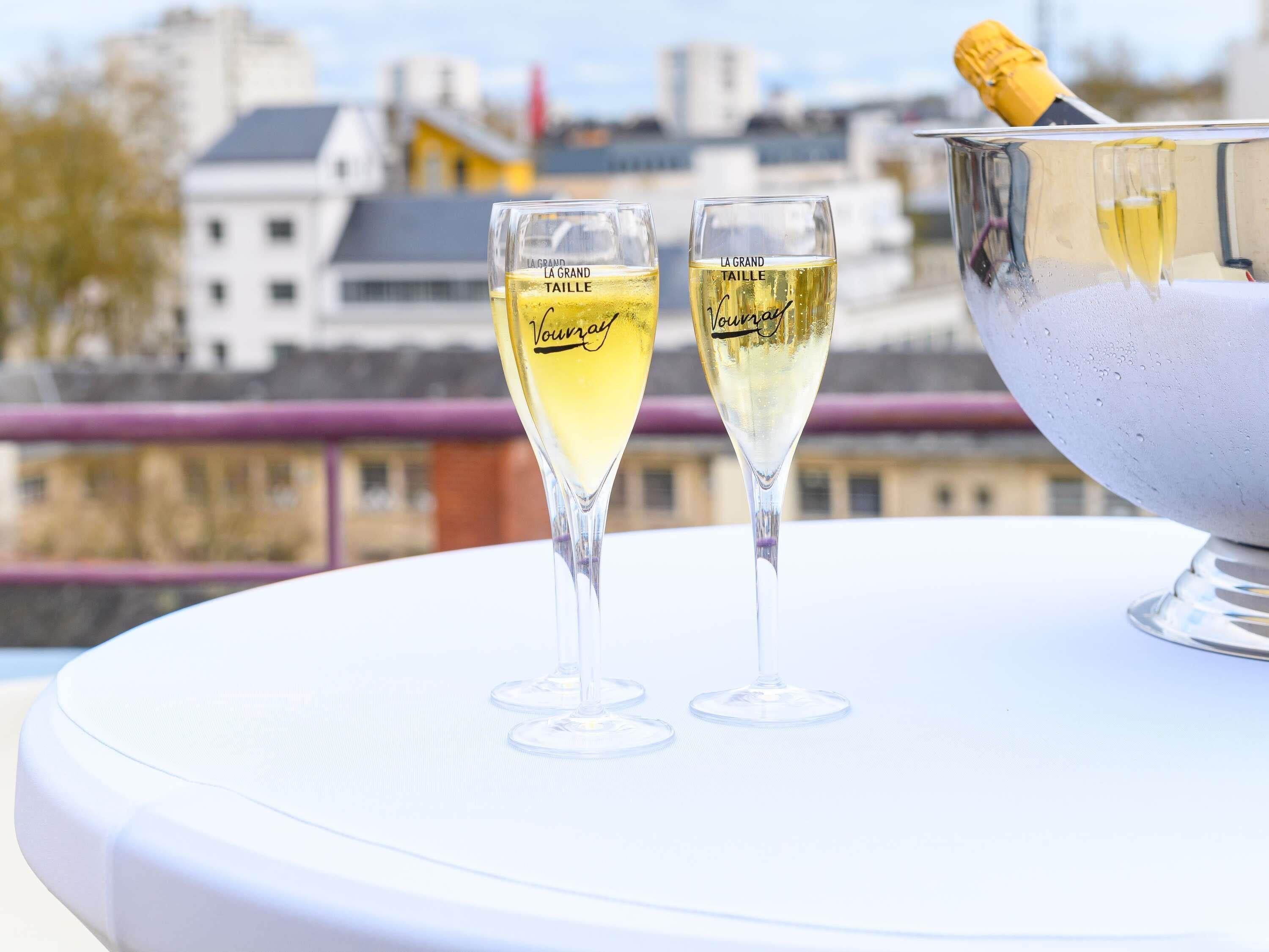 Deux coupes à champagne sur une table blanche, avec une vue sur la ville en arrière-plan.