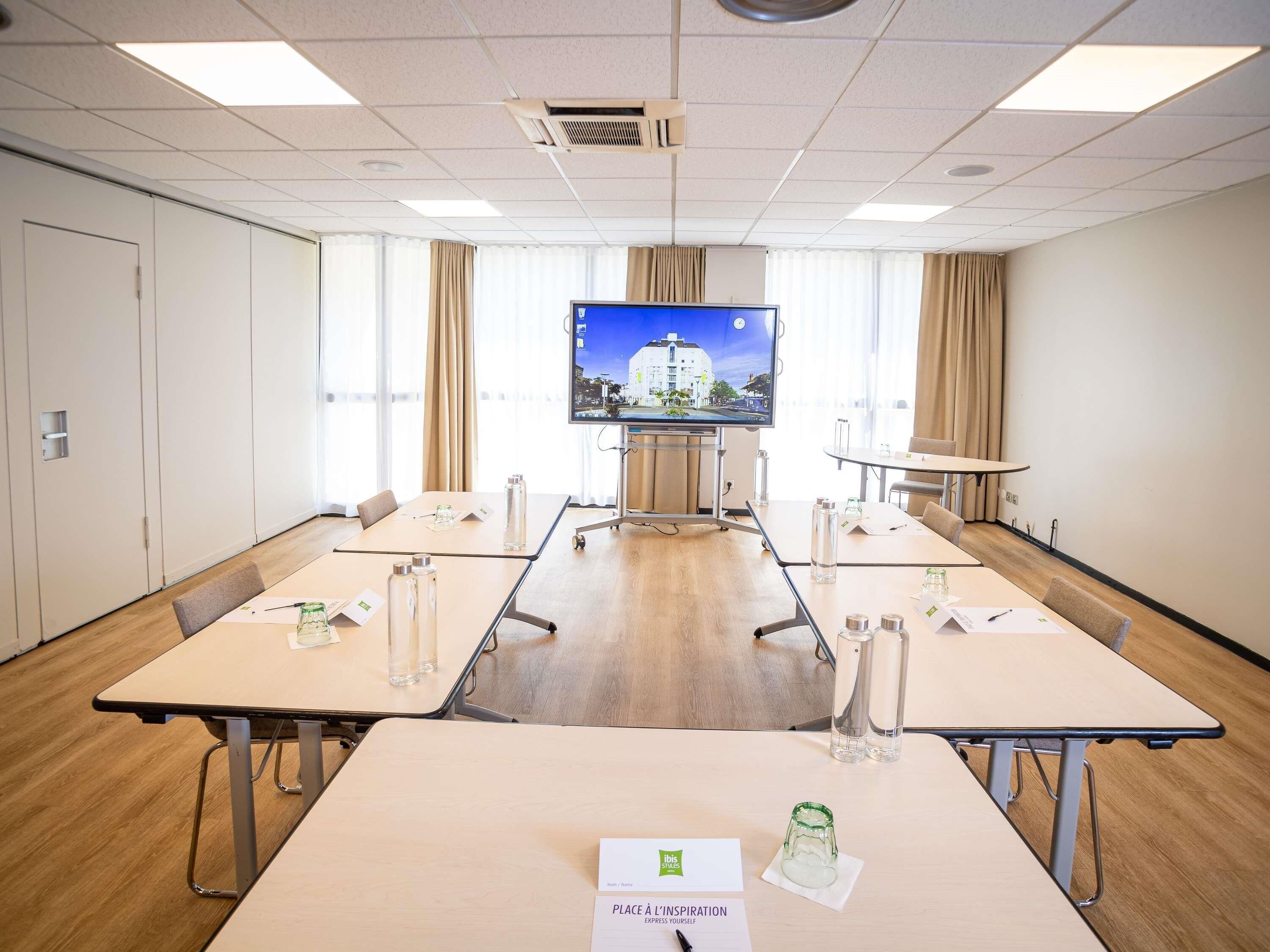 Une salle de conférence équipée d’un grand écran, de plusieurs tables, de chaises et d’un présentoir à cartes de nom posé sur la table.