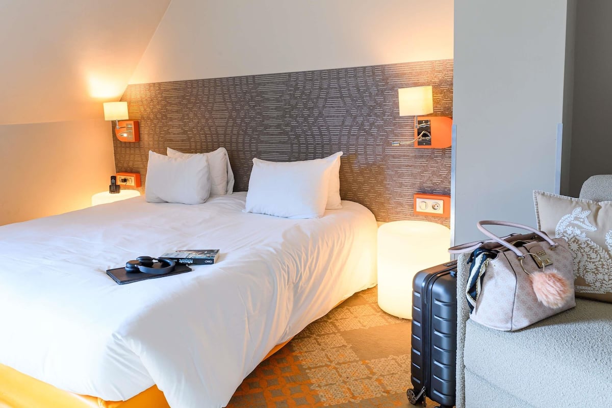 A hotel room with a large bed, bedside lamps, a bedside table with a phone, and a suitcase on the floor.