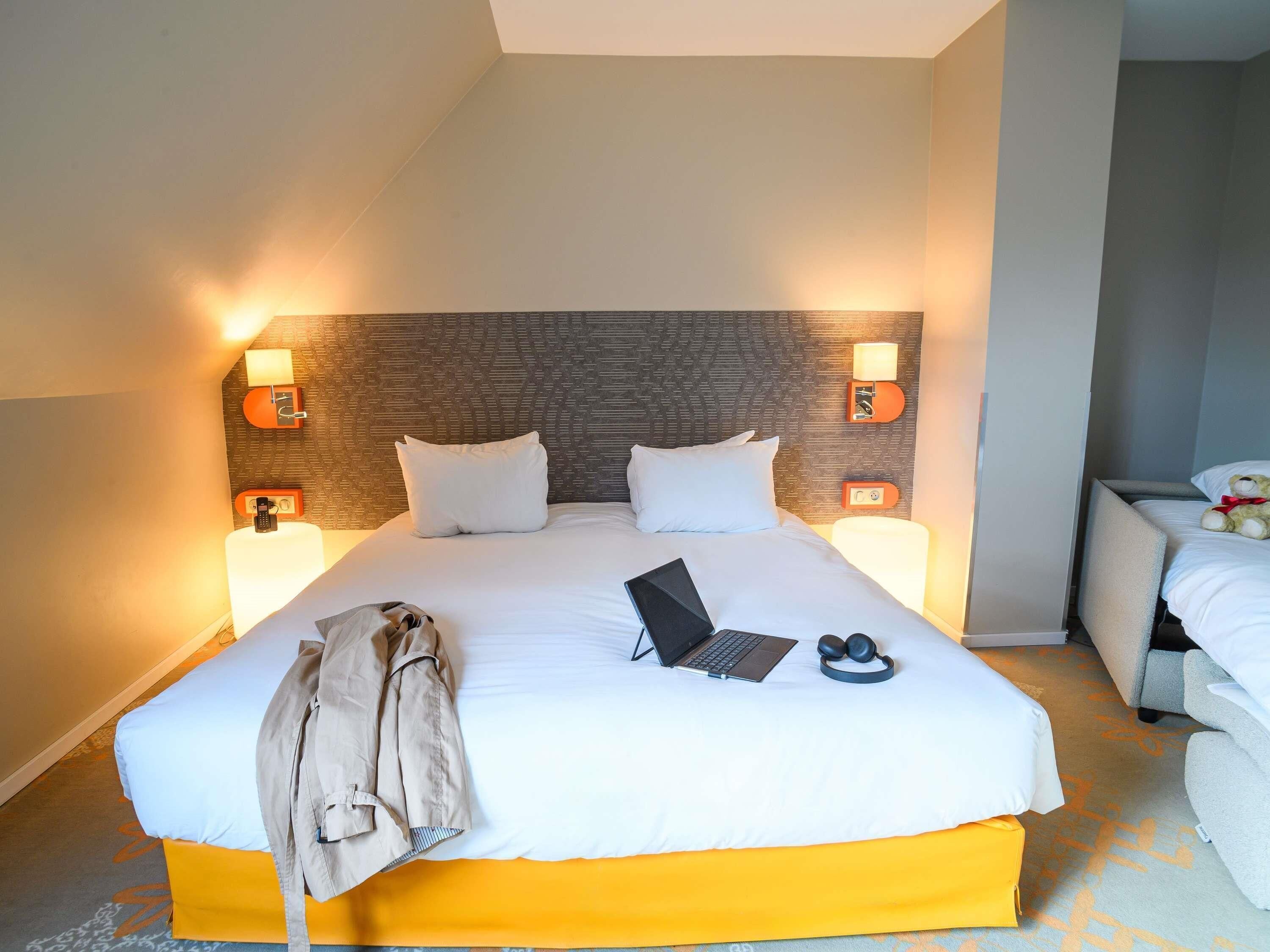 A hotel room with a large bed, a laptop, headphones, and a jacket on the bed.