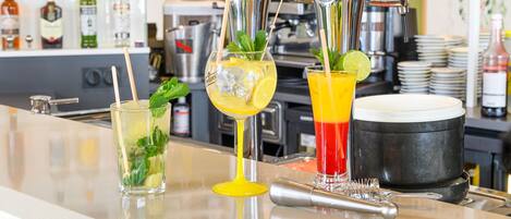 Una zona de bar con tres grifos sirviendo diferentes bebidas, un coctelero y una pila de platos al fondo.