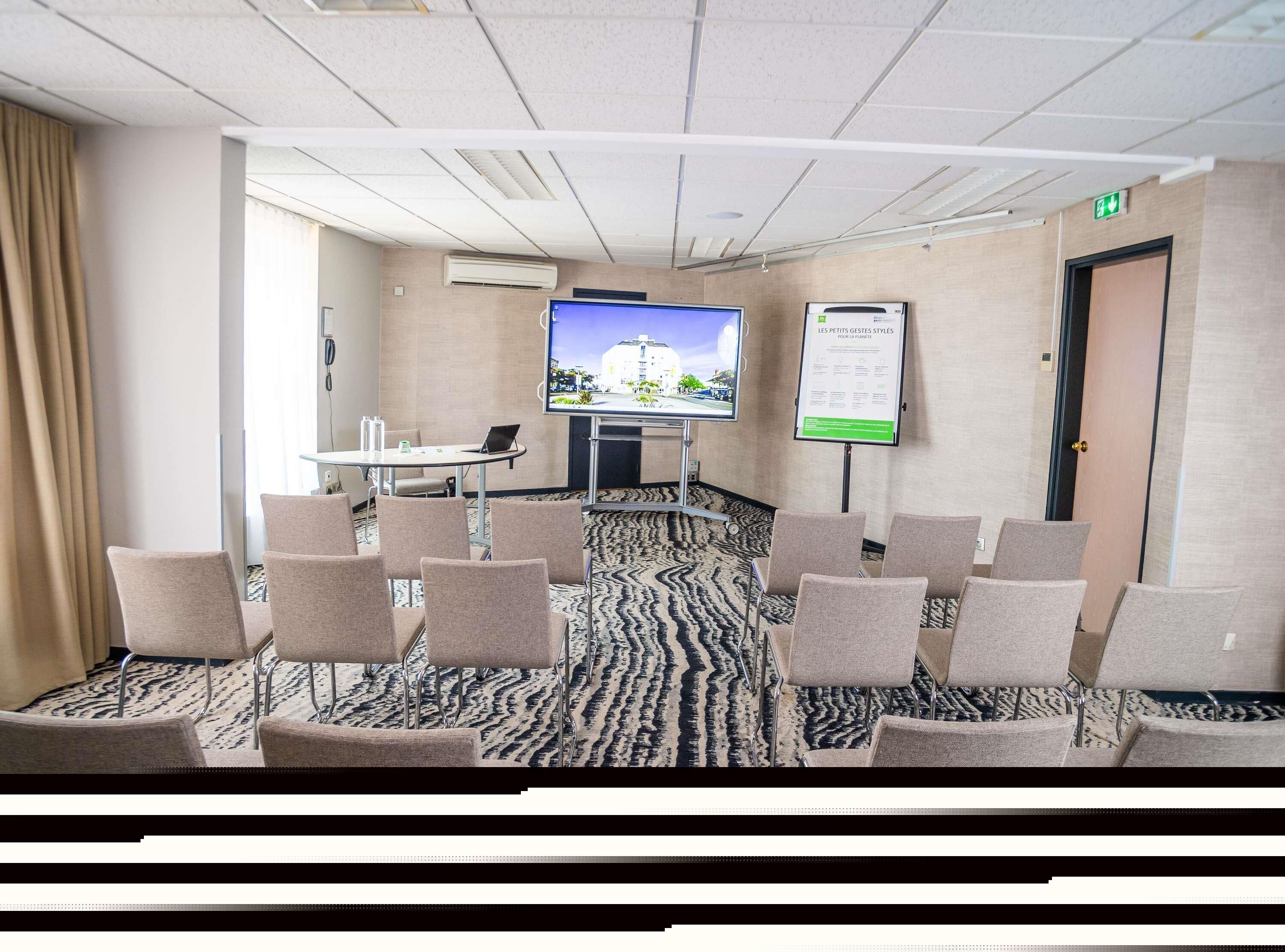 A conference room with a large screen, a table with chairs, and a carpeted floor.