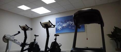 A fitness room with three stationary bikes, a treadmill, and a wall-mounted water fountain.