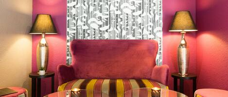 A modern living room with a red sofa, two lamps, a glass coffee table, and striped ottomans.