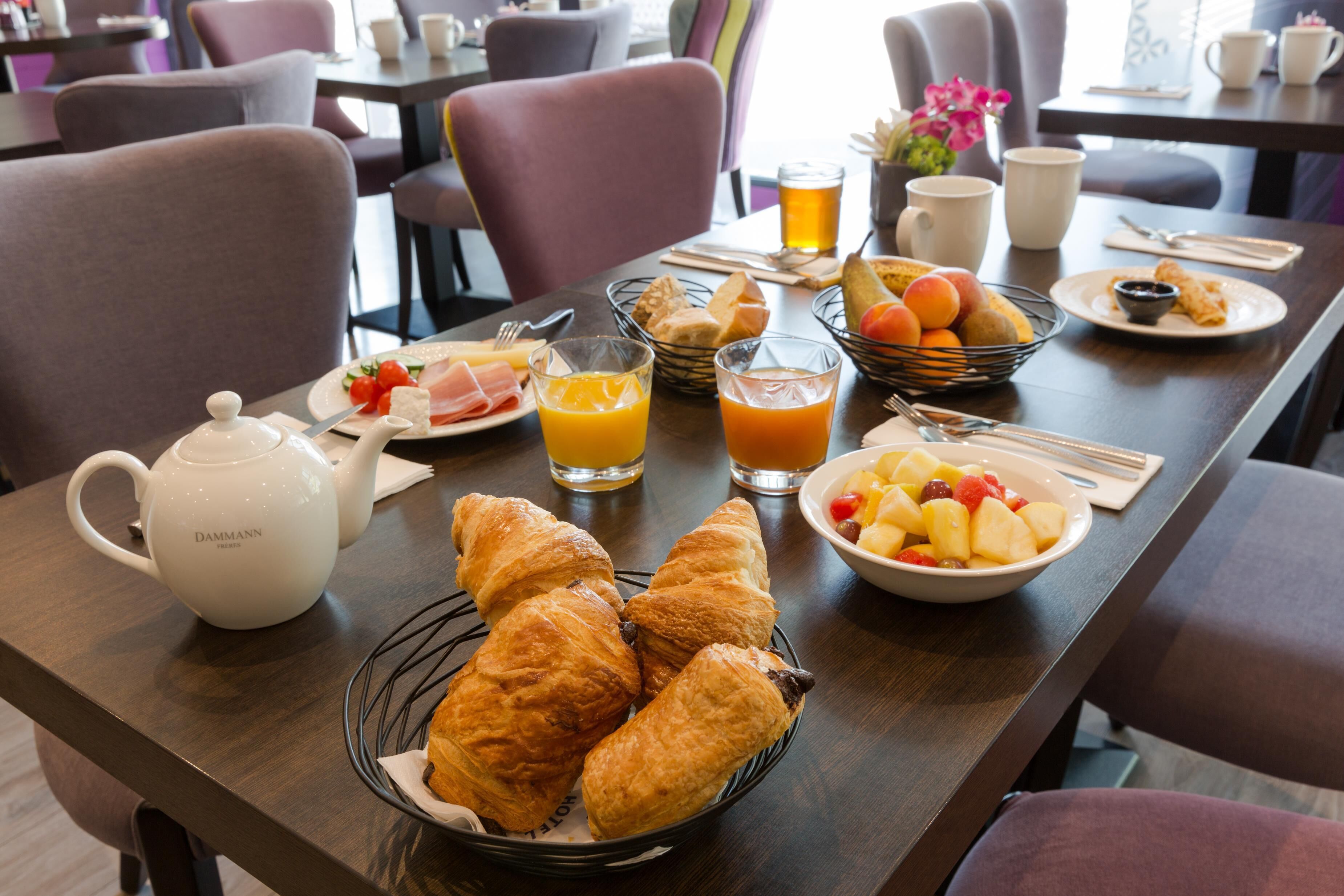 Une table dressée pour le petit-déjeuner, avec des croissants, des fruits, du jus et une théière.