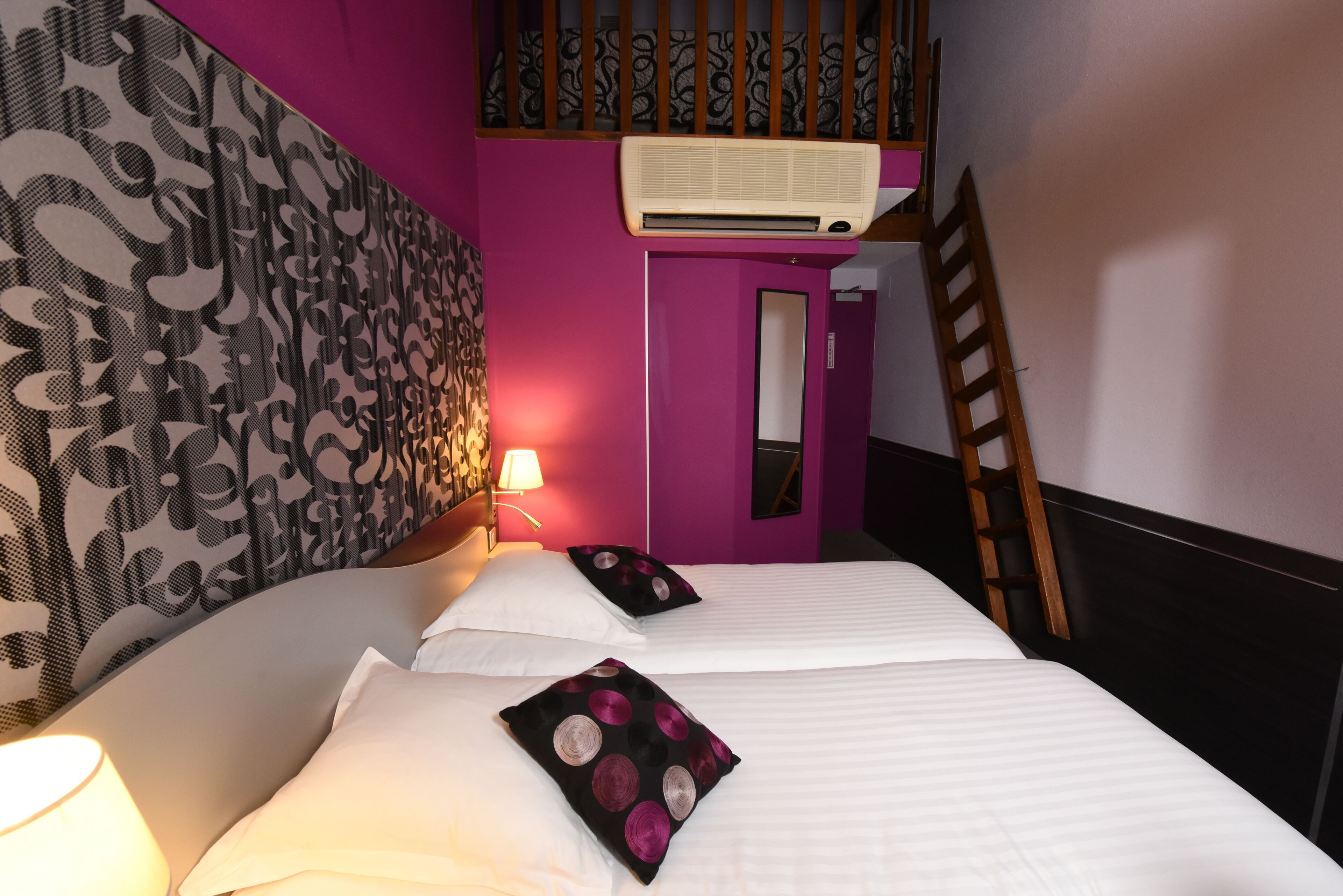 A room with two beds, a wall-mounted air conditioner, a wooden ladder, and a patterned wall.