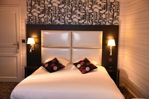 A hotel room with a large bed, two bedside lamps, and a patterned wallpaper.