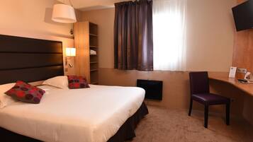 A hotel room with a large bed, a desk, a chair, a TV, a bookshelf, and a window with curtains.