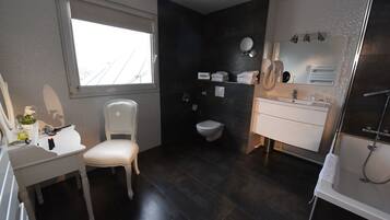A modern bathroom with a dark tiled floor, a white vanity with a mirror, a white chair, a toilet, and a shower area.