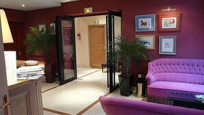 A lobby with a purple sofa, a reception desk, and framed artwork on the walls. - Hôtel Cardinal Rive Gauche (Paris)