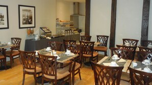 A dining area with wooden chairs and tables, a buffet counter with food and beverages, and framed pictures on the walls. - Hôtel Cardinal Rive Gauche (Paris)