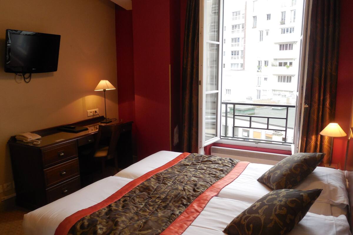 A hotel room with a bed, a desk, a chair, a television, and a window with a view of buildings.