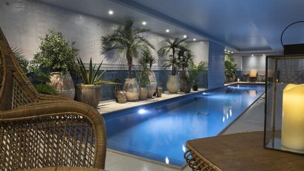 An indoor swimming pool with a tiled floor, surrounded by wicker furniture and large potted plants. - Hôtel Cardinal Rive Gauche (Paris)