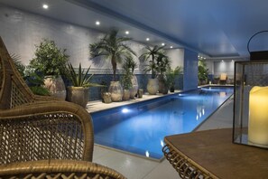 An indoor swimming pool with a tiled floor, surrounded by wicker furniture and large potted plants. - Hôtel Cardinal Rive Gauche (Paris)