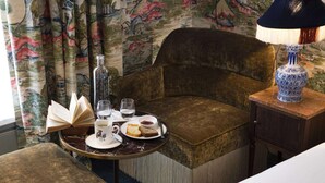 A cozy room with a plush armchair, a small round table with a book, glasses, and a plate of food. - Hôtel Cardinal Rive Gauche (Paris)