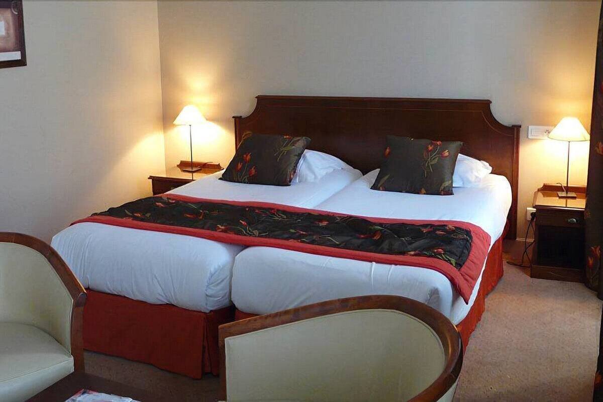 A double bed with a red and black floral bedspread, two bedside lamps, and a wooden headboard.