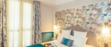 Une chambre d’hôtel avec un lit, un plateau de petit-déjeuner, une table de chevet avec une lampe et un papier peint à motifs floraux.