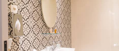A bathroom with patterned tiles, a pedestal sink, a mirror, and a bathtub.