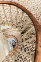 Eine Wendeltreppe mit Holzwand und weißen Balustraden, die zu einer Ebene weiter unten führt.