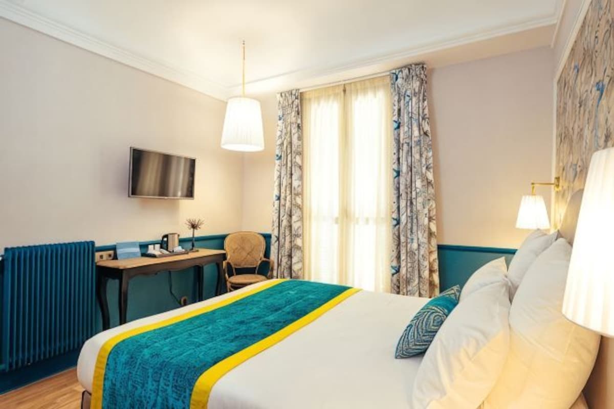 Een hotelkamer met een bed, bureau, stoel, televisie en gordijnen.