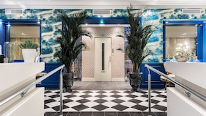 A hotel lobby with a checkered floor, a reception desk, and two large potted plants.