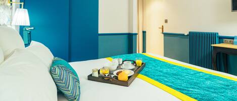 Una habitación de hotel con cama, una bandeja de desayuno, una pared azul y una ventana.