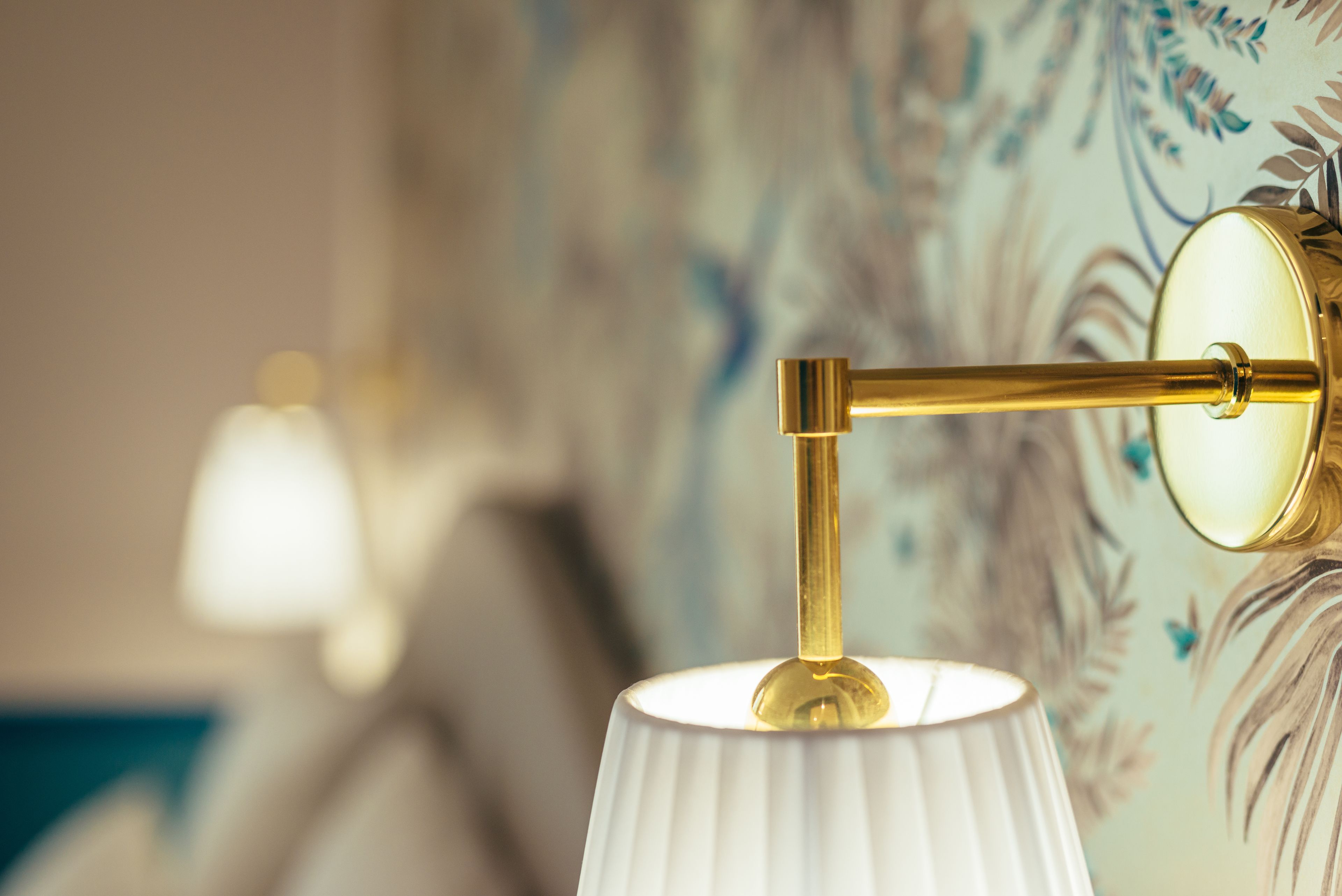 A close-up of a wall-mounted lamp with a white lampshade and a gold-colored fixture.