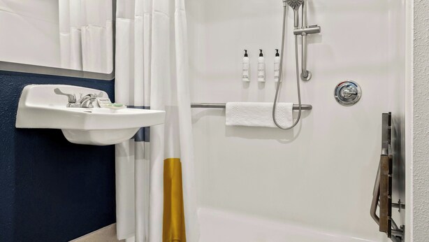 A bathroom with a white sink, a shower with a handheld showerhead, and a towel rack. - City Express By Marriott Freeport (Freeport)