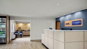 Et hotelreceptionsområde med en reception, et køleskab fyldt med drikkevarer, et siddeområde med stole og en væg med et fiskebensmønster.