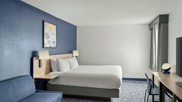 A hotel room with a bed, a desk, a chair, a TV, and a painting on the wall.
