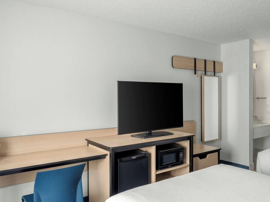 Habitación de hotel con cama, escritorio con televisor, microondas, cubo de basura pequeño y espejo.