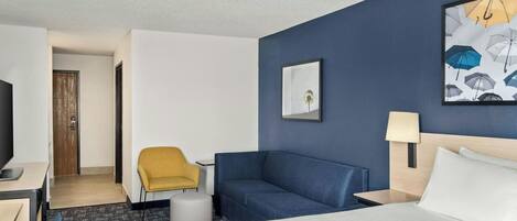Ein Hotelzimmer mit Bett, Schreibtisch, Stuhl, Nachttisch, Lampe und einem Bild an der Wand.
