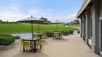 Un espace extérieur aménagé en terrasse, avec des tables et des chaises, des parasols et une vue sur un paysage verdoyant.