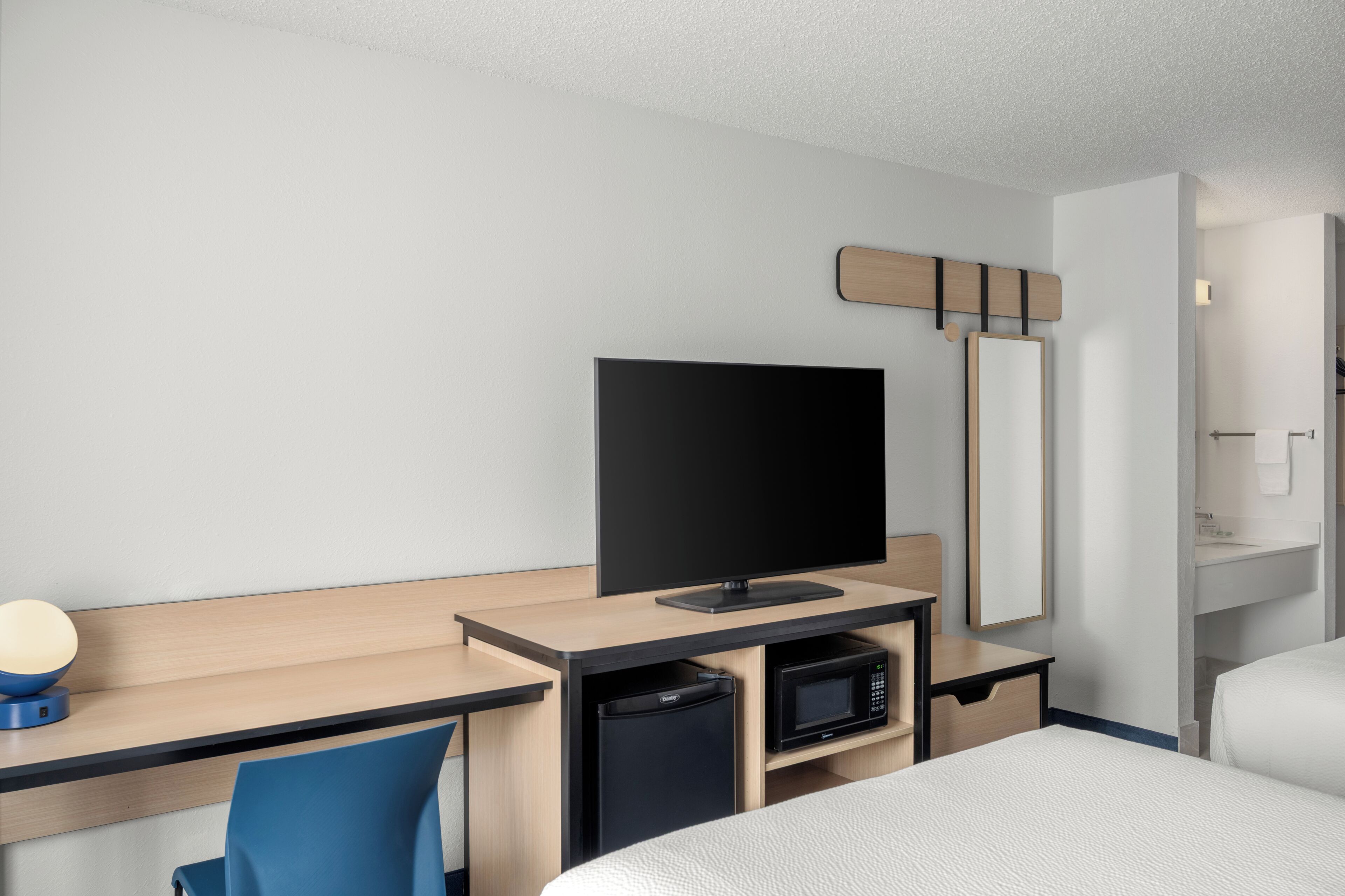 Habitación de hotel con cama, escritorio con televisor de pantalla plana, microondas, basurero pequeño y espejo.